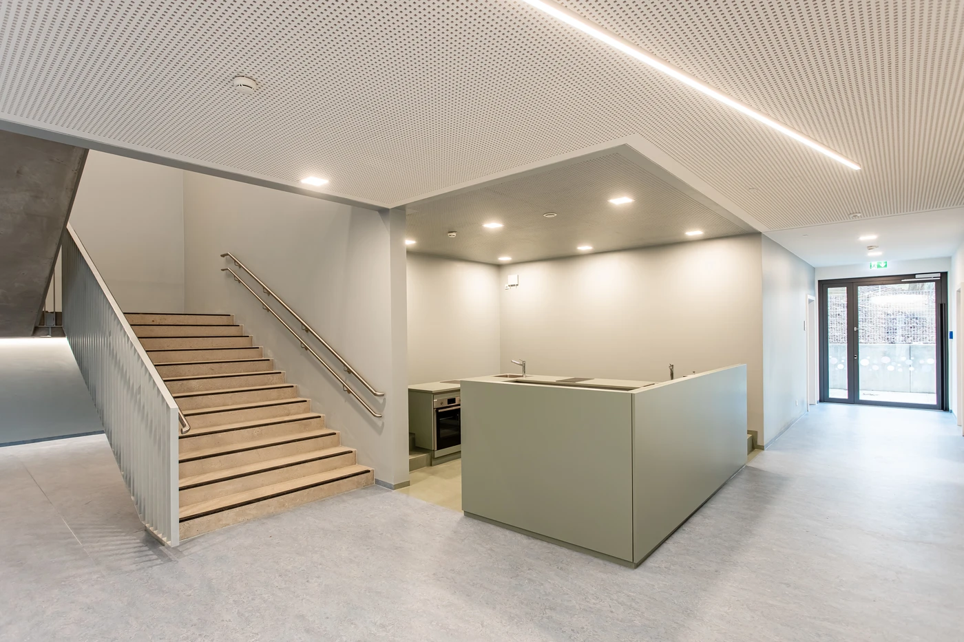 Moderner, minimalistischer Innenraum in Schorndorf mit hellen Wänden, einer Treppe mit Geländer, einer kleinen Küchenzeile und Glastüren, die Tageslicht hereinlassen. Das klare und aufgeräumte Design spiegelt die durchdachte Gestaltung und die sorgfältige Projektentwicklung im gesamten Bereich wider.