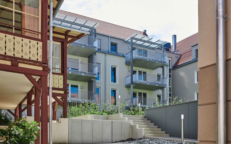 Modernes Mehrfamilienhaus mit zahlreichen Balkonen, großen Fenstern und einem Satteldach; im Vordergrund sind ein Treppenhaus und eine Grünanlage zu sehen – ein vorbildliches Projekt von SCHATZ Architektur, das die Kompetenz in der Generalplanung über alle Leistungsphasen hinweg unter Beweis stellt.