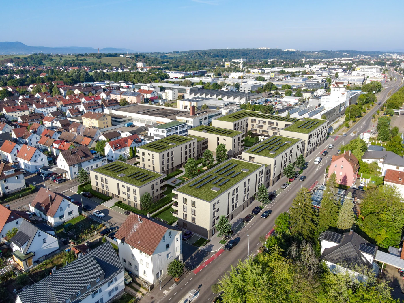 Luftaufnahme einer modernen Wohnanlage mit begrünten Dächern, die im Rahmen einer umfassenden Generalplanung in Schorndorf entstanden ist und von älteren Häusern, Straßen sowie nahegelegenen Industriegebäuden umgeben ist – unter strahlend blauem Himmel.