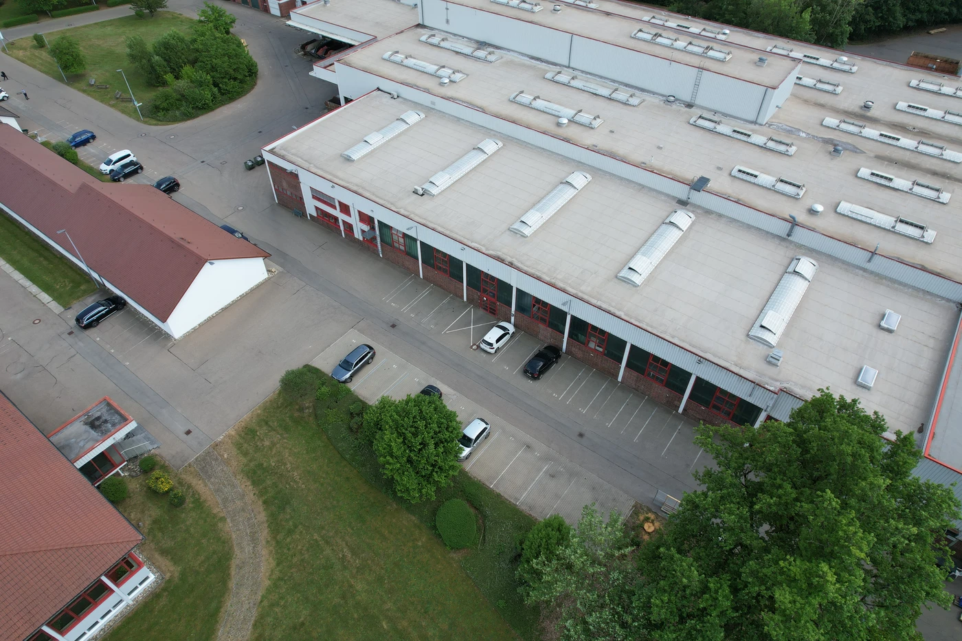 Luftaufnahme eines großen Industriegebäudes mit weißem Dach in Schorndorf, angrenzendem Parkplatz mit mehreren Autos und umgebender Grünanlage – ein eindrucksvolles Beispiel für Projektentwicklung, das die verschiedenen Leistungsphasen verdeutlicht.