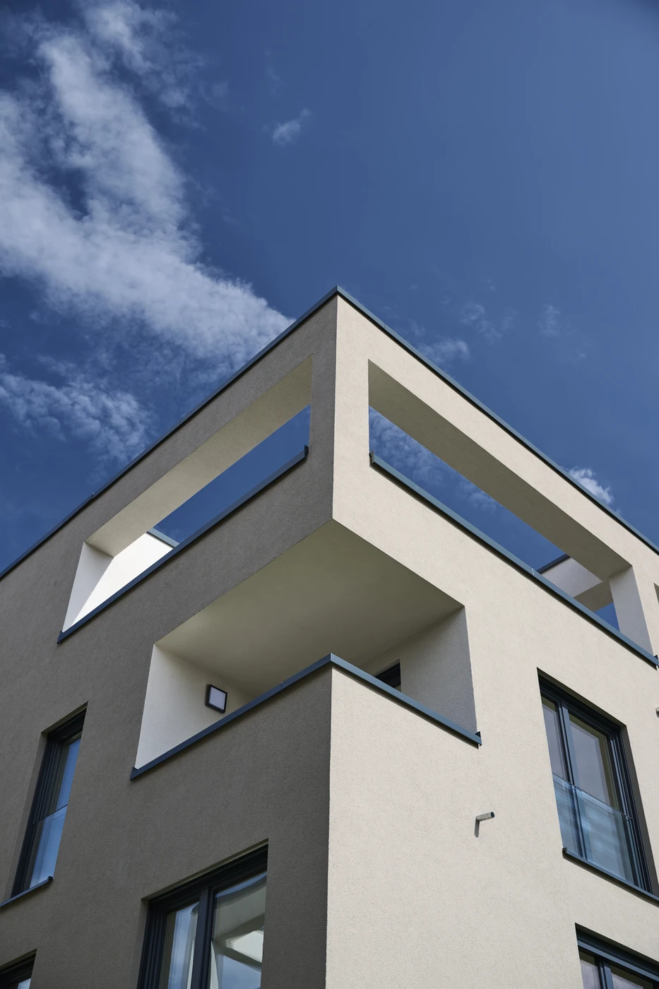 Projekte Ein modernes, weißes, mehrstöckiges Gebäude mit großen rechteckigen Balkonen und Glasgeländern vor dem Hintergrund eines blauen Himmels mit vereinzelten Wolken – ein eindrucksvolles Beispiel für die Generalplanung von SCHATZ Architektur in Schorndorf.