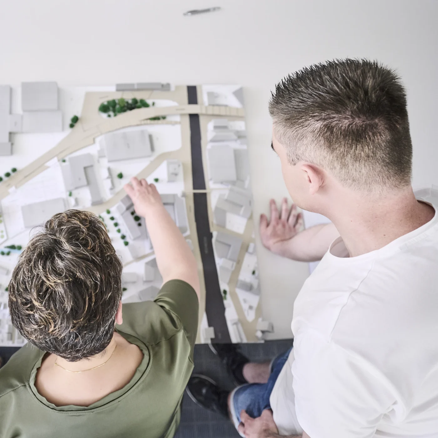 Was uns ausmacht Zwei Personen betrachten ein Architekturmodell eines Stadtviertels mit Gebäuden, Straßen und Bäumen aus der Vogelperspektive und besprechen es, wobei sie Aspekte der Generalplanung und der Projektentwicklung im gesamten Entwurfsprozess berücksichtigen.