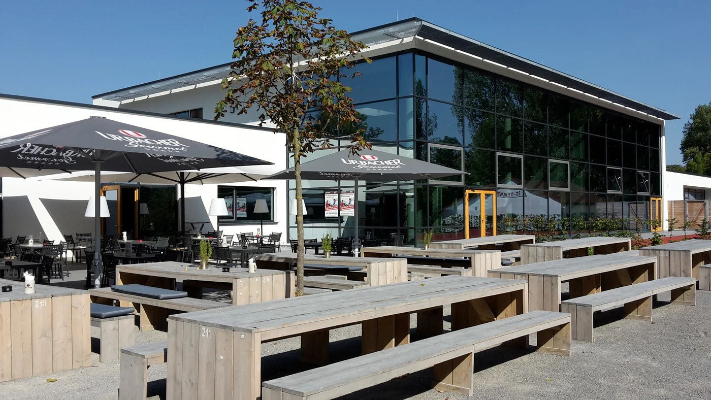 Ein Sitzbereich im Freien mit Holztischen und -bänken, der von großen Sonnenschirmen beschattet wird und an einem sonnigen Tag vor einem modernen Glasgebäude liegt – ein Raum, der durch sorgfältige Planung und Projektentwicklung durchdacht gestaltet wurde.