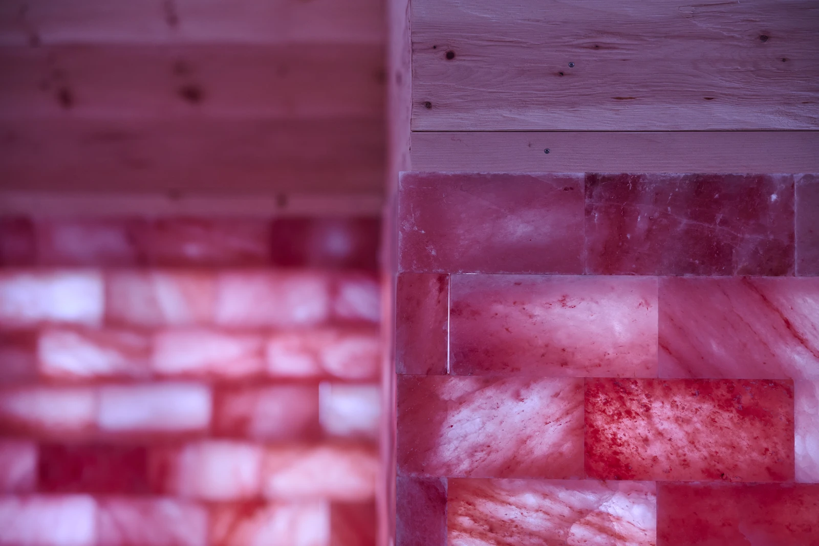 Nahaufnahme einer Wand aus rosa Himalaya-Salzziegeln, wobei sanfte Beleuchtung eine warme und beruhigende Atmosphäre schafft.