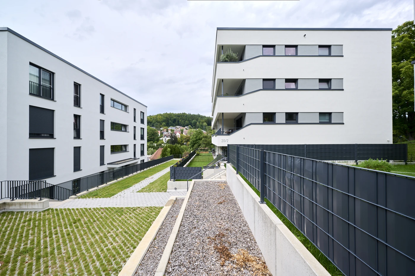 Startseite Moderne weiße Mehrfamilienhäuser mit Balkonen und schwarzen Fensterläden, die durch einen mit Gras und Kies bepflanzten Fußgängerweg voneinander getrennt sind, zeugen von einer durchdachten Projektentwicklung in Schorndorf und sind von Zäunen und Grünflächen umgeben.