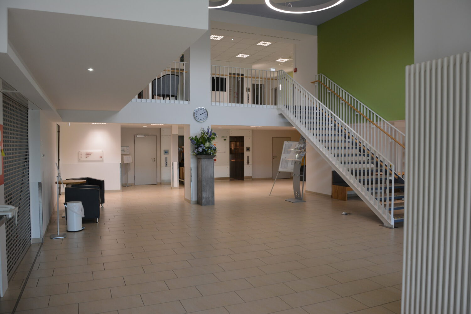 Geräumige Eingangshalle mit zentraler Treppe, Fliesenboden und einer grünen Akzentwand.