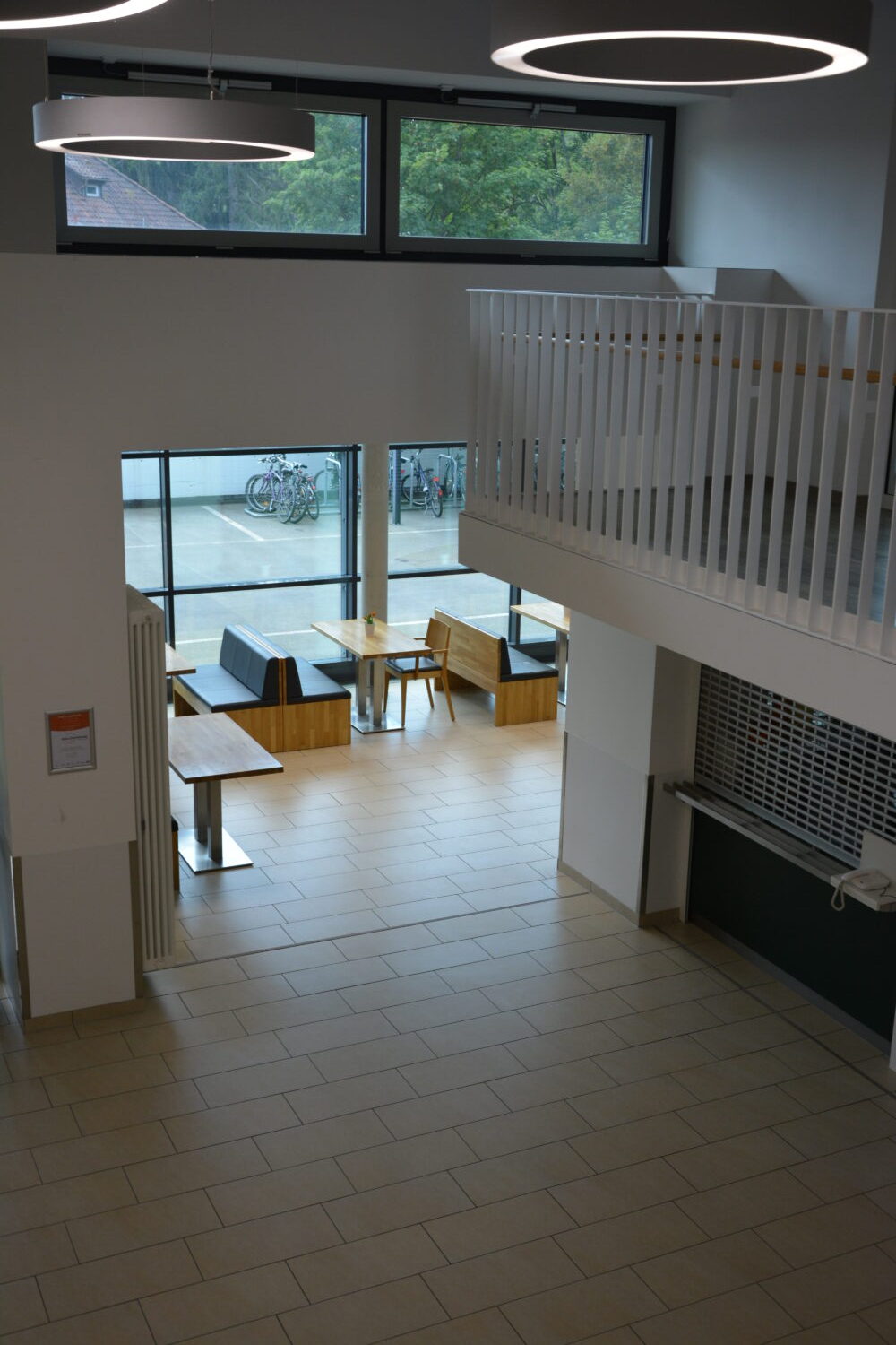 Ein Blick in den Innenraum einer Lobby mit Sitznischen, Tischen und einem Blick auf einen Fahrradständer durch große Fenster.